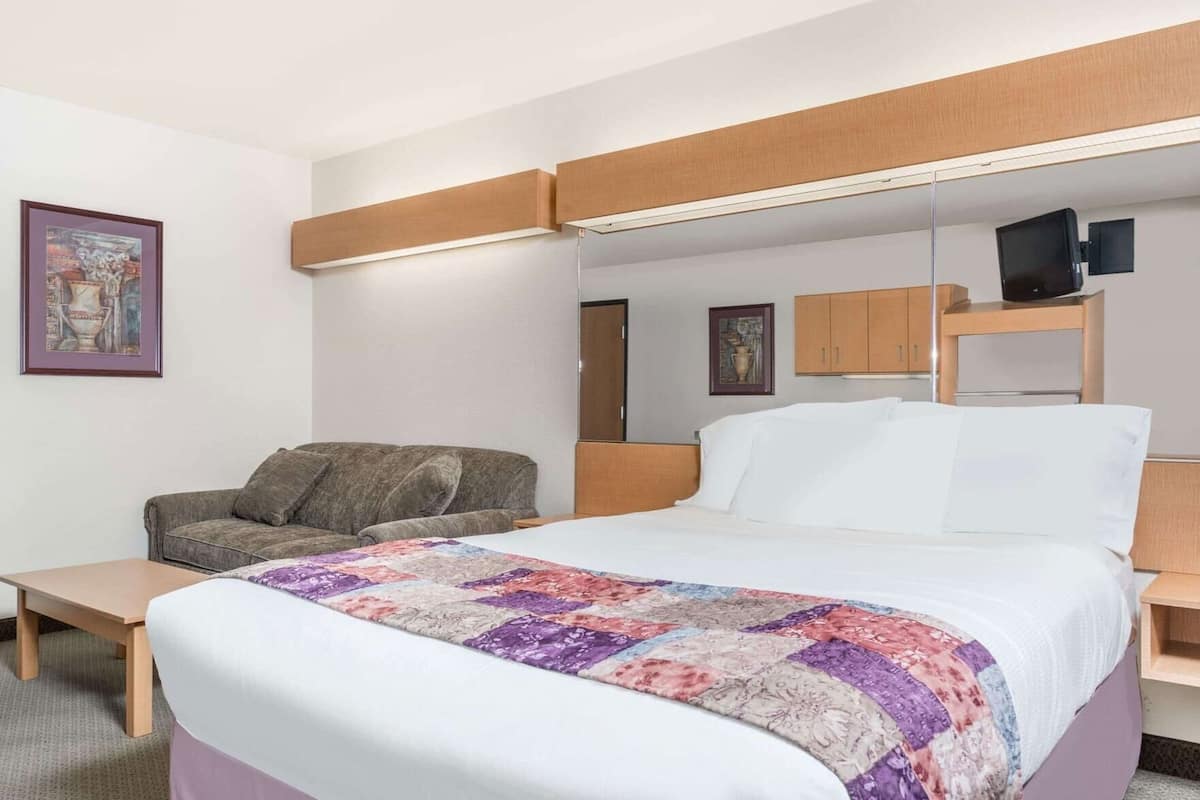 A hotel room with a bed, a sofa, a desk, a mirror, and a television.