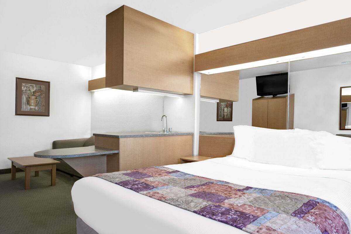 A hotel room with a bed, a small desk, a chair, a mirror, and a television.
