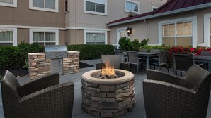 An outdoor patio with a stone fire pit, wicker furniture, and a barbecue grill. - Residence Inn by Marriott Chico (Chico)