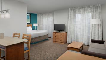 A hotel room with a bed, a television on a wooden stand, a desk with a chair, a sofa, and a window with curtains.