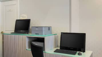 Una oficina de hotel con un escritorio equipado con una laptop, una impresora y una computadora de escritorio.