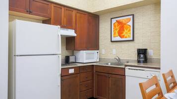 A compact kitchen with wooden cabinets, a white refrigerator, a microwave, a dishwasher, and a coffee maker.
