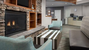 A living room with a stone fireplace, a flat-screen TV, and a seating area with a striped coffee table. - Residence Inn by Marriott Chico (Chico)