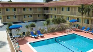 A hotel with a pool area, including lounge chairs and umbrellas. - Motel 6 Riviera Beach, FL (West Palm Beach)
