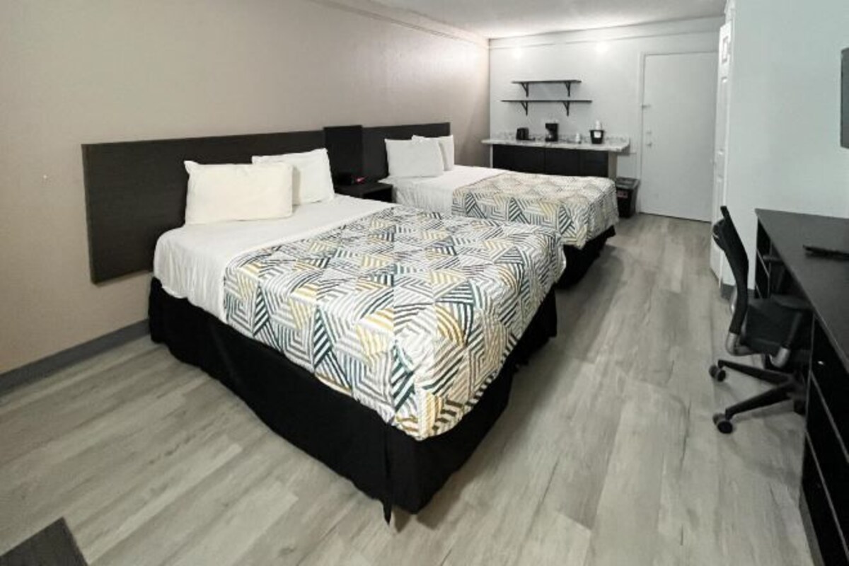 A hotel room with two beds, a desk, and a kitchenette.