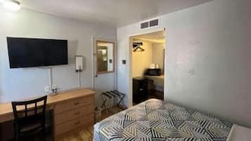Habitación de hotel pequeña con cama, escritorio, silla, cómoda, televisor y baño visible a través de una puerta abierta.