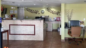 A reception area with a counter, a clock, and a desk with a computer and chair. - Motel 6 Riviera Beach, FL (West Palm Beach)