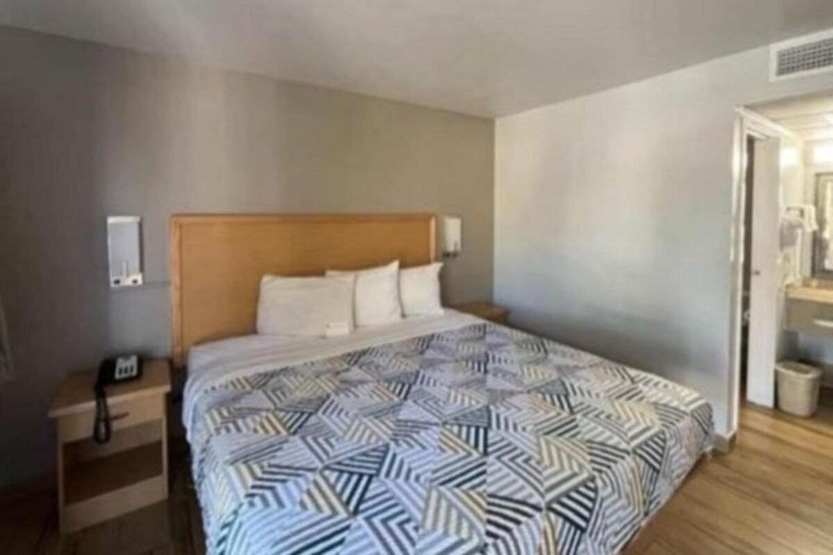 A hotel room with a large bed, a nightstand, a bedside table, and a door leading to a bathroom.
