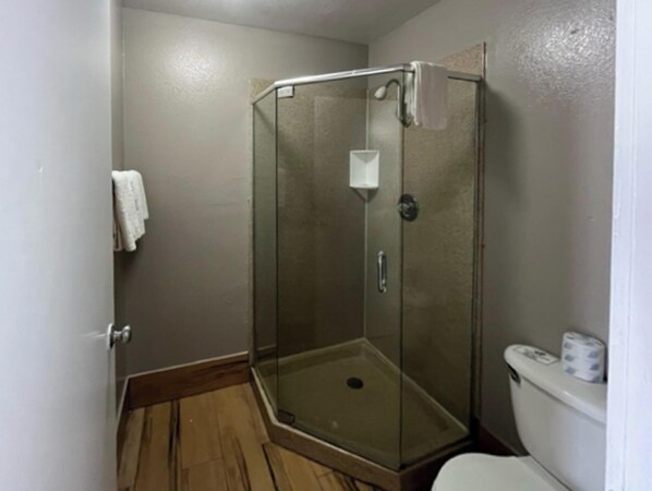 Un baño pequeño con cabina de ducha de vidrio, inodoro y una toalla blanca colgada en la pared.