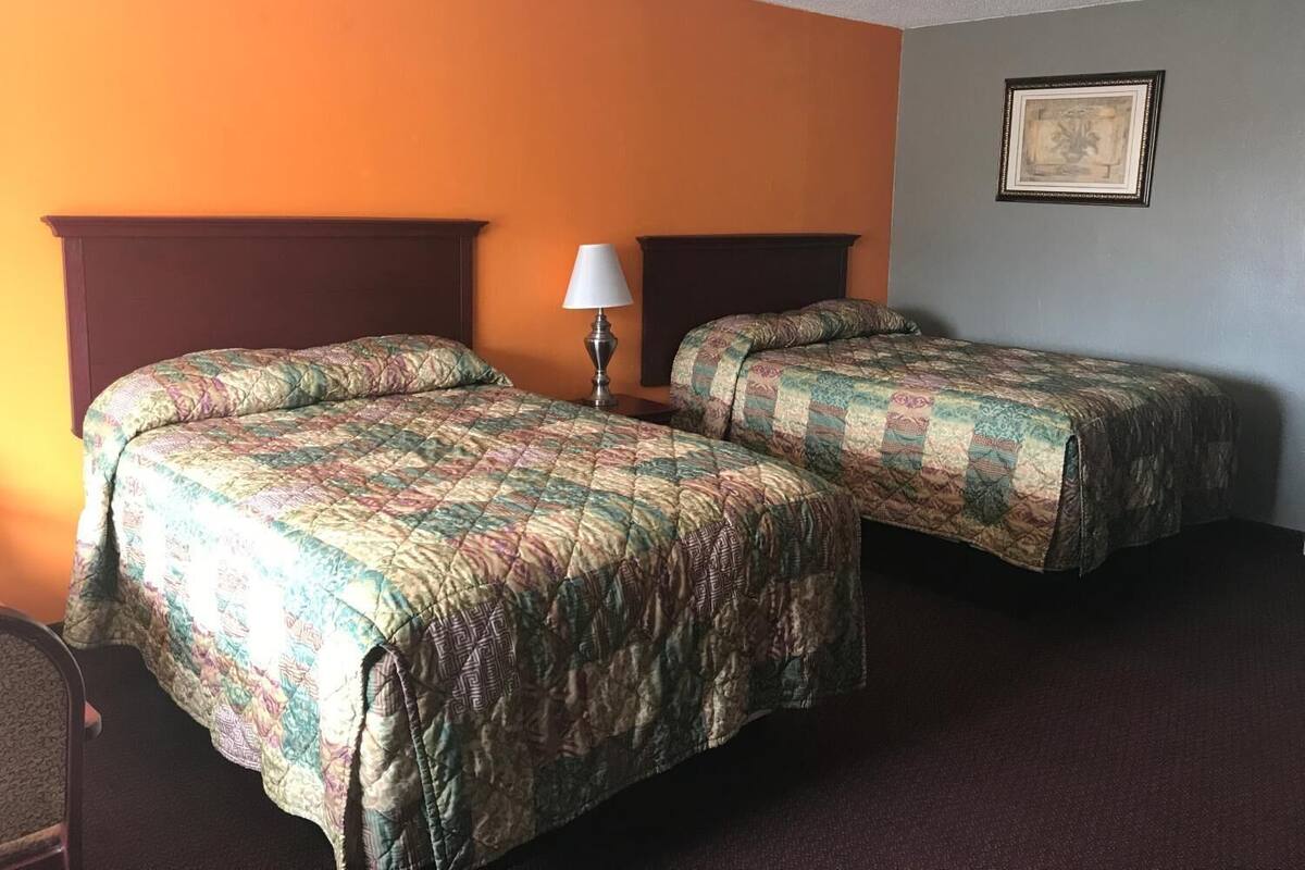 A hotel room with two beds, a nightstand with a lamp, and a framed picture on the wall.