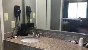 A bathroom with a granite countertop sink, a large mirror, hair dryers, and a window with curtains. - Express Inn - Bay City (Bay City)