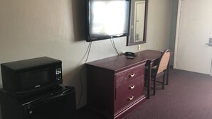 A room with a television mounted on the wall, a wooden dresser with drawers, a microwave on top of a refrigerator, and a chair. - Express Inn - Bay City (Bay City)