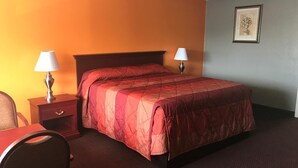 A hotel room with a bed, two bedside tables with lamps, a chair, and a framed picture on the wall. - Express Inn - Bay City (Bay City)