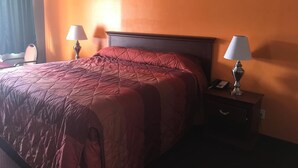A hotel room with a large bed, two bedside lamps, a nightstand, and a window with curtains. - Express Inn - Bay City (Bay City)