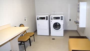 A laundry room with two washing machines, a table, two chairs, and a bench.