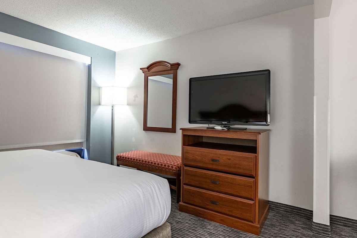 A hotel room with a bed, a wooden dresser with a television, a bench, and a lamp.