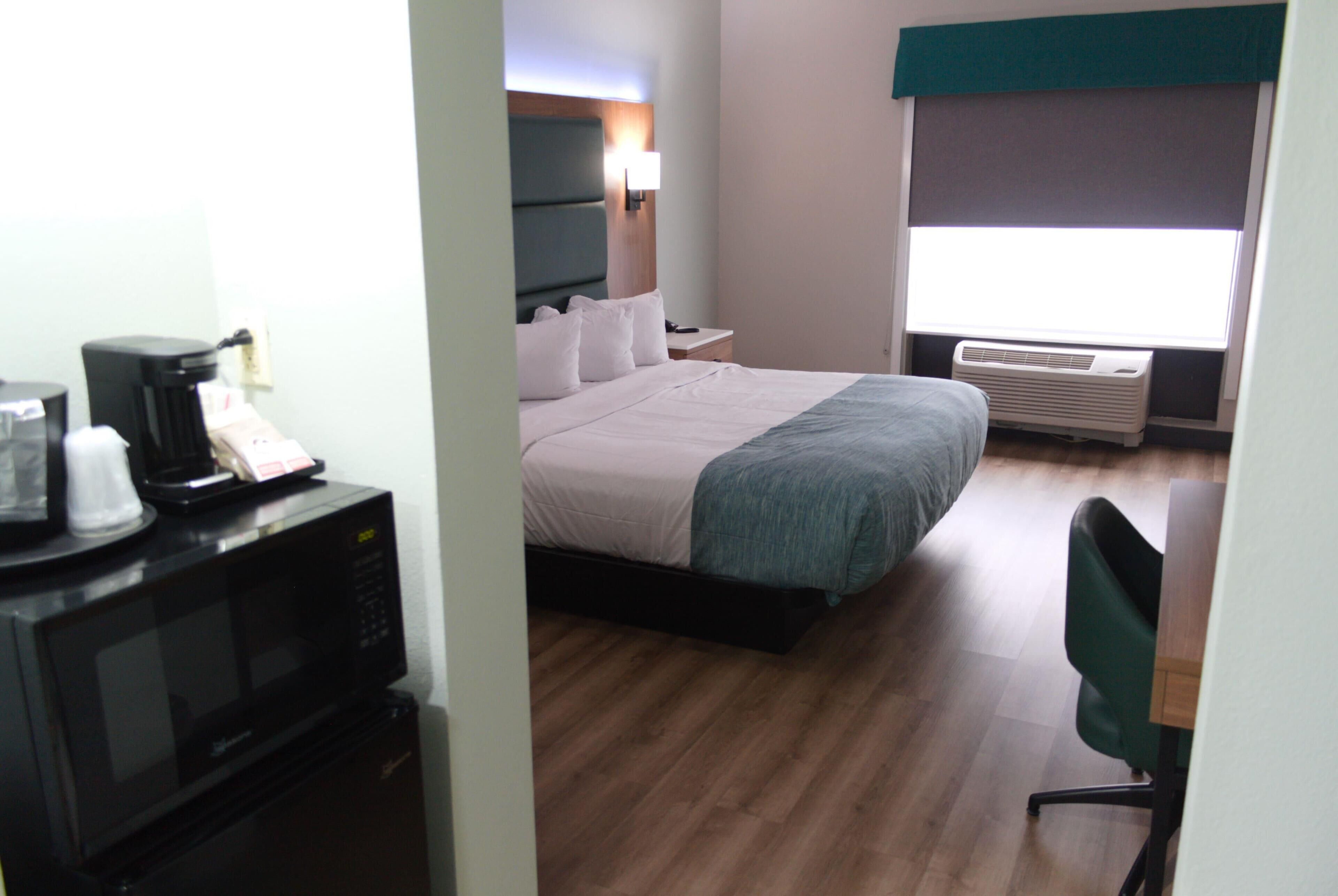 A hotel room with a bed, a desk with a chair, a microwave, and an air conditioner.