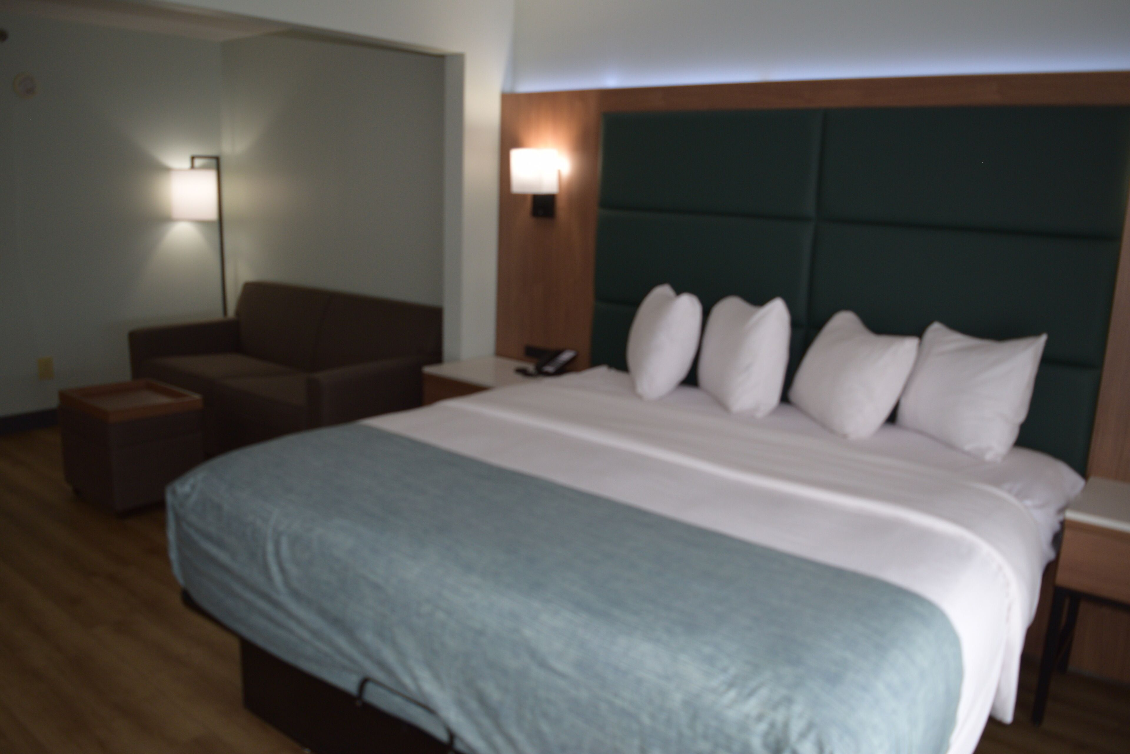 Una habitación de hotel con una cama grande, un sofá, una mesita de noche y una lámpara fijada a la pared.
