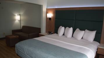 Una habitación de hotel con una cama grande, un sofá, una mesita de noche y una lámpara fijada a la pared.