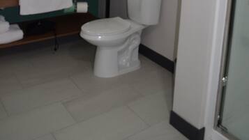 Un baño con inodoro blanco, lavamanos con espejo y zona de ducha.