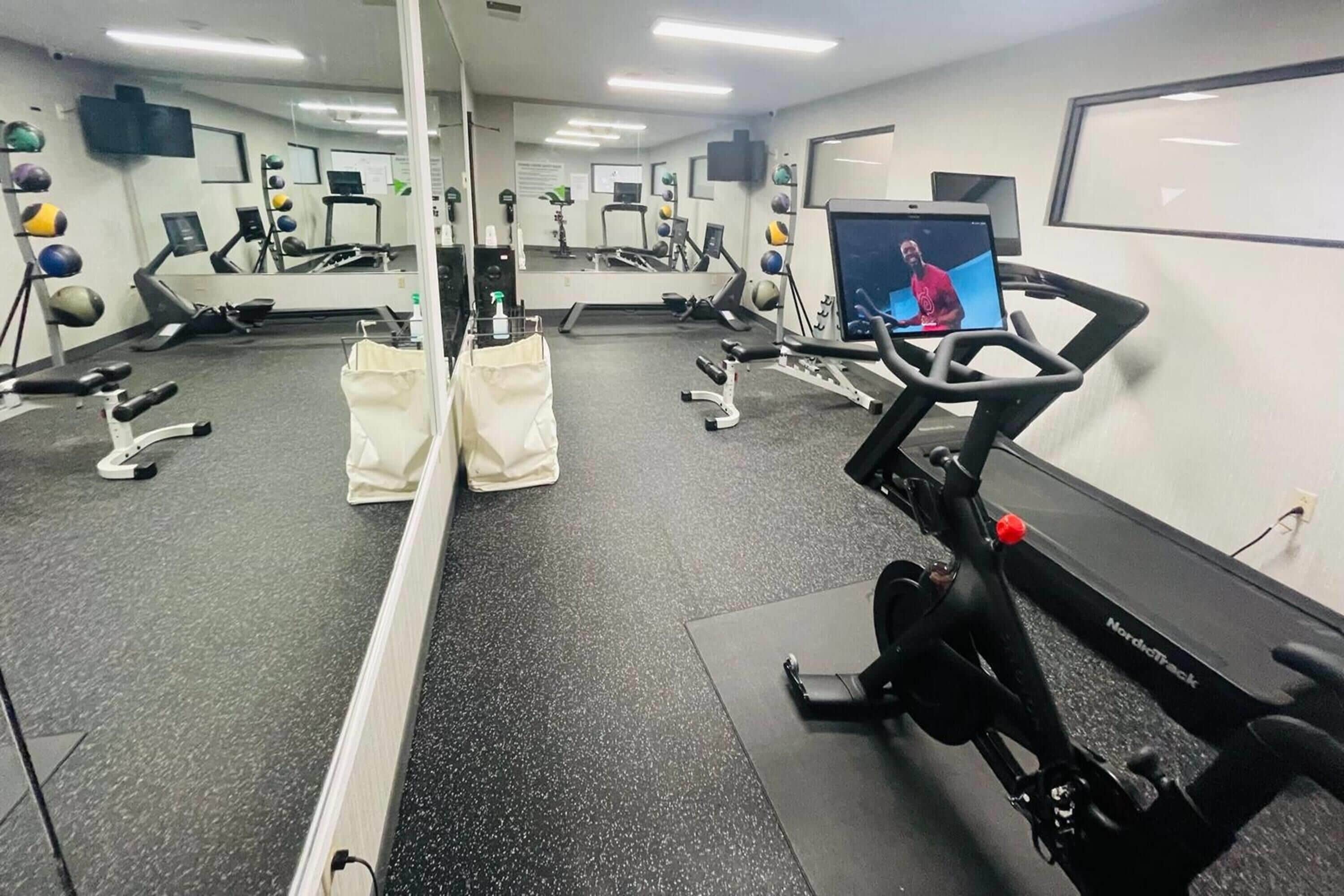 A gym with cardio equipment, mirrors, and a TV screen.