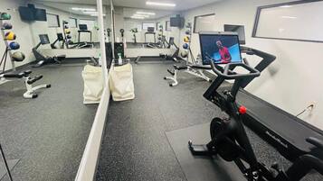 A gym with cardio equipment, mirrors, and a TV screen.