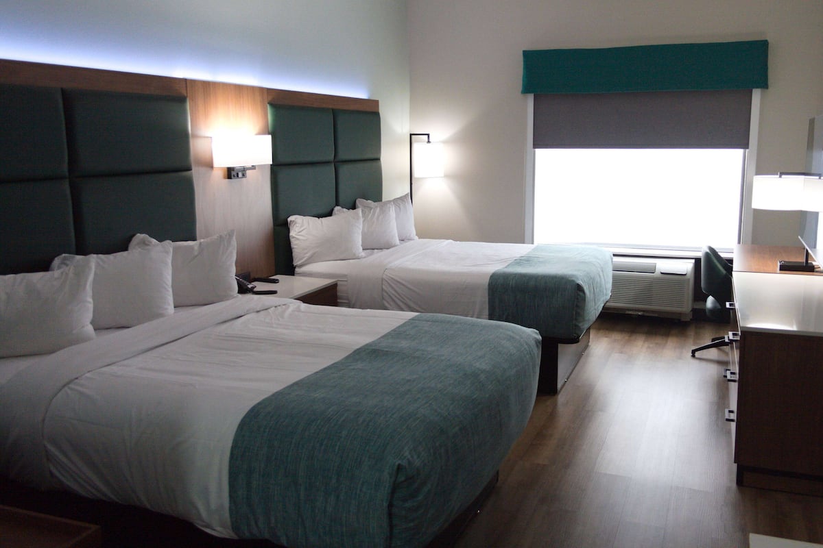 A hotel room with two beds, a desk, and a window with a view.