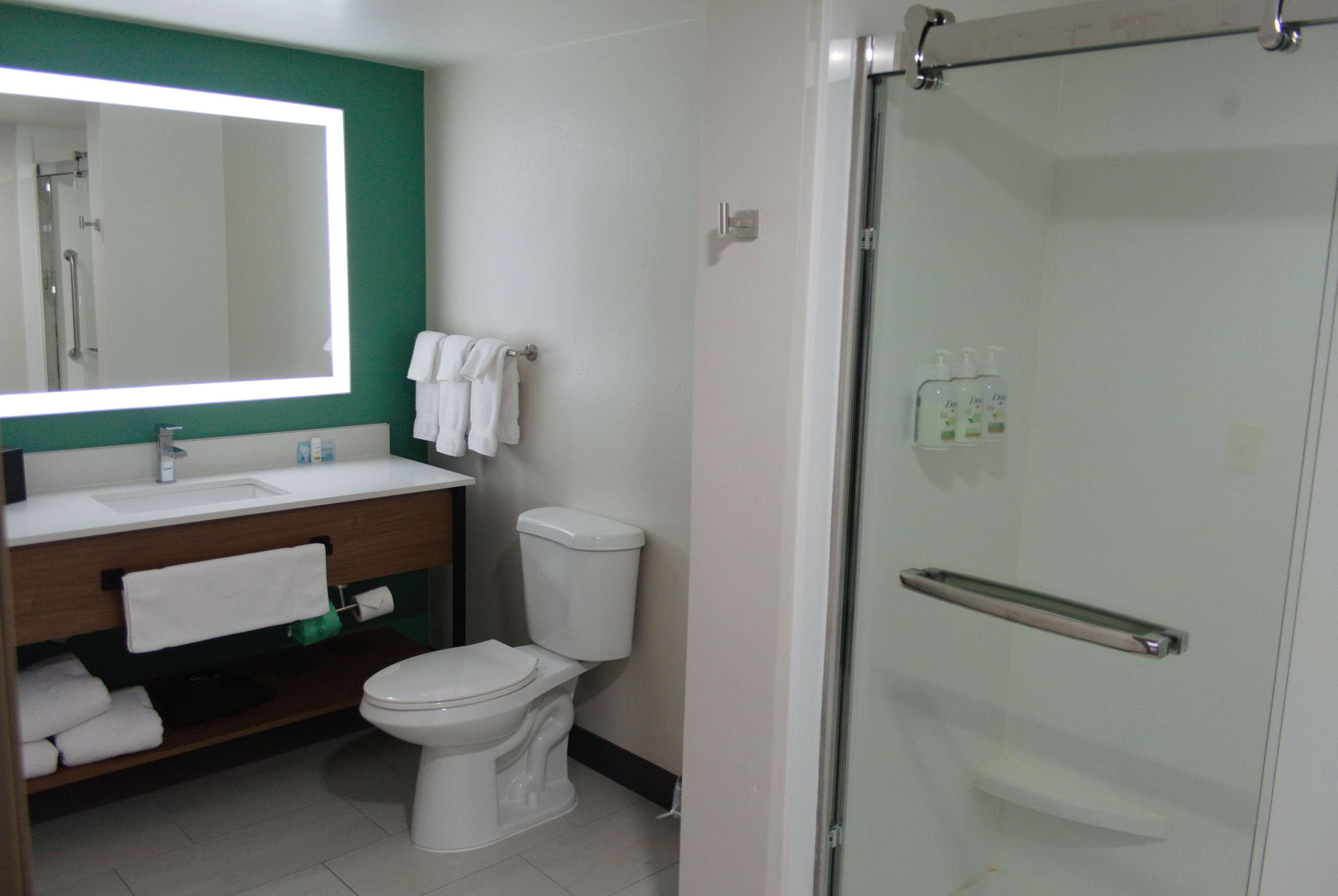Een moderne badkamer met een douchecabine van glas, een wit toilet, een wastafel met spiegel en een badkamermeubel met handdoeken.