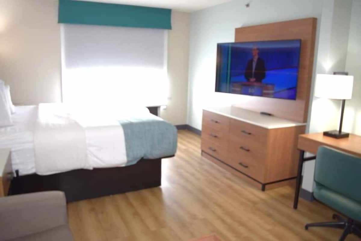 A hotel room with a bed, a TV, a desk, and a chair.