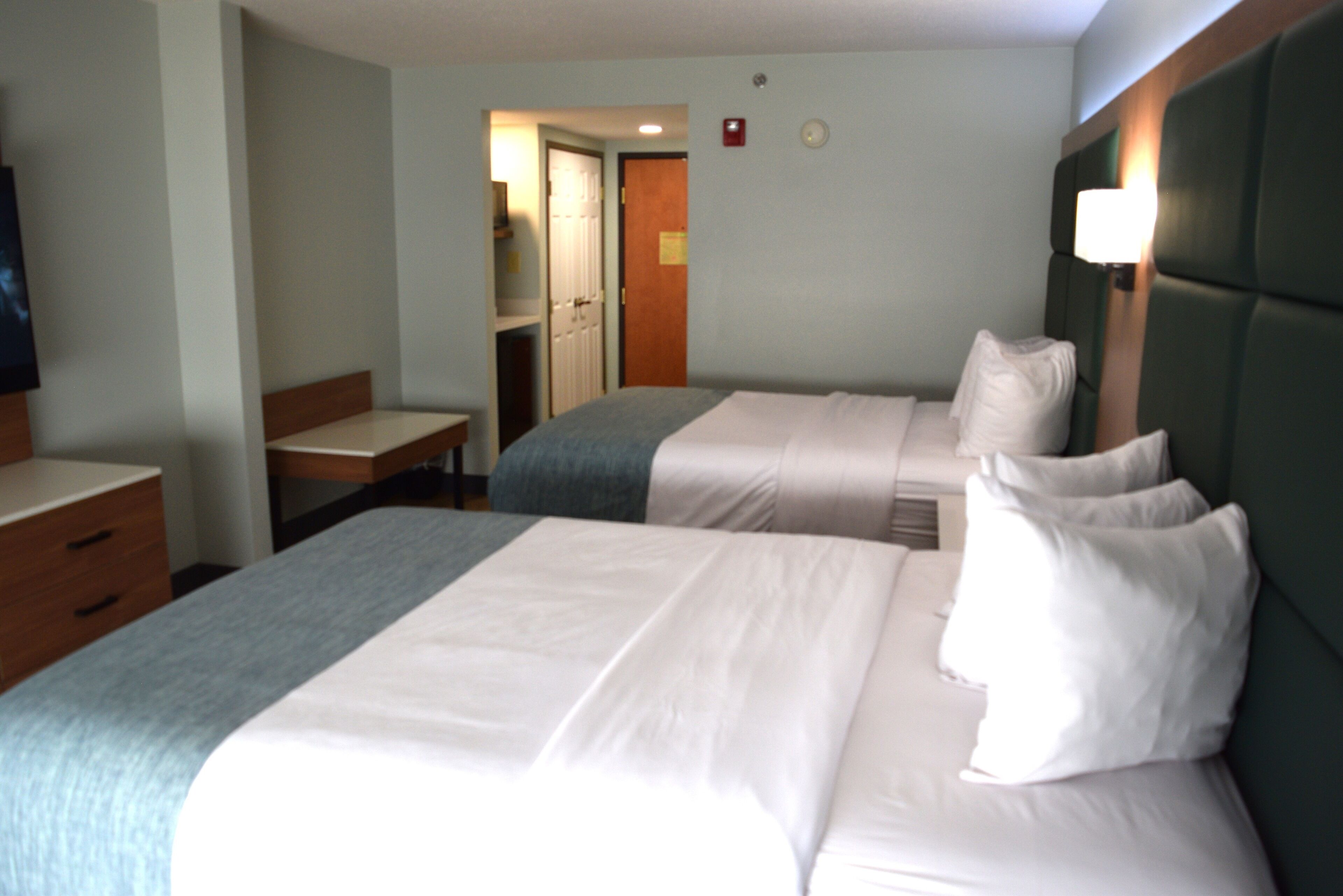 A hotel room with two beds, a desk, and a television.