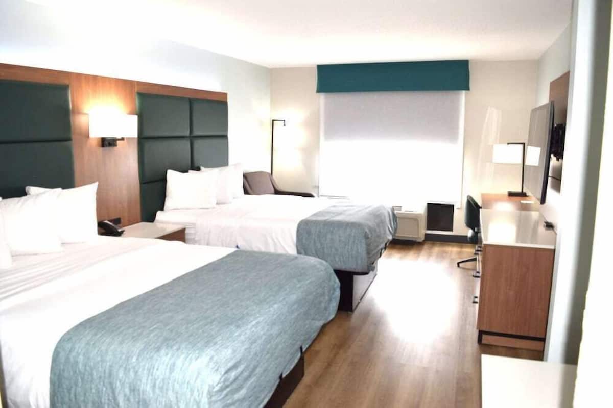 A hotel room with two beds, a desk, a chair, a TV, and a window.