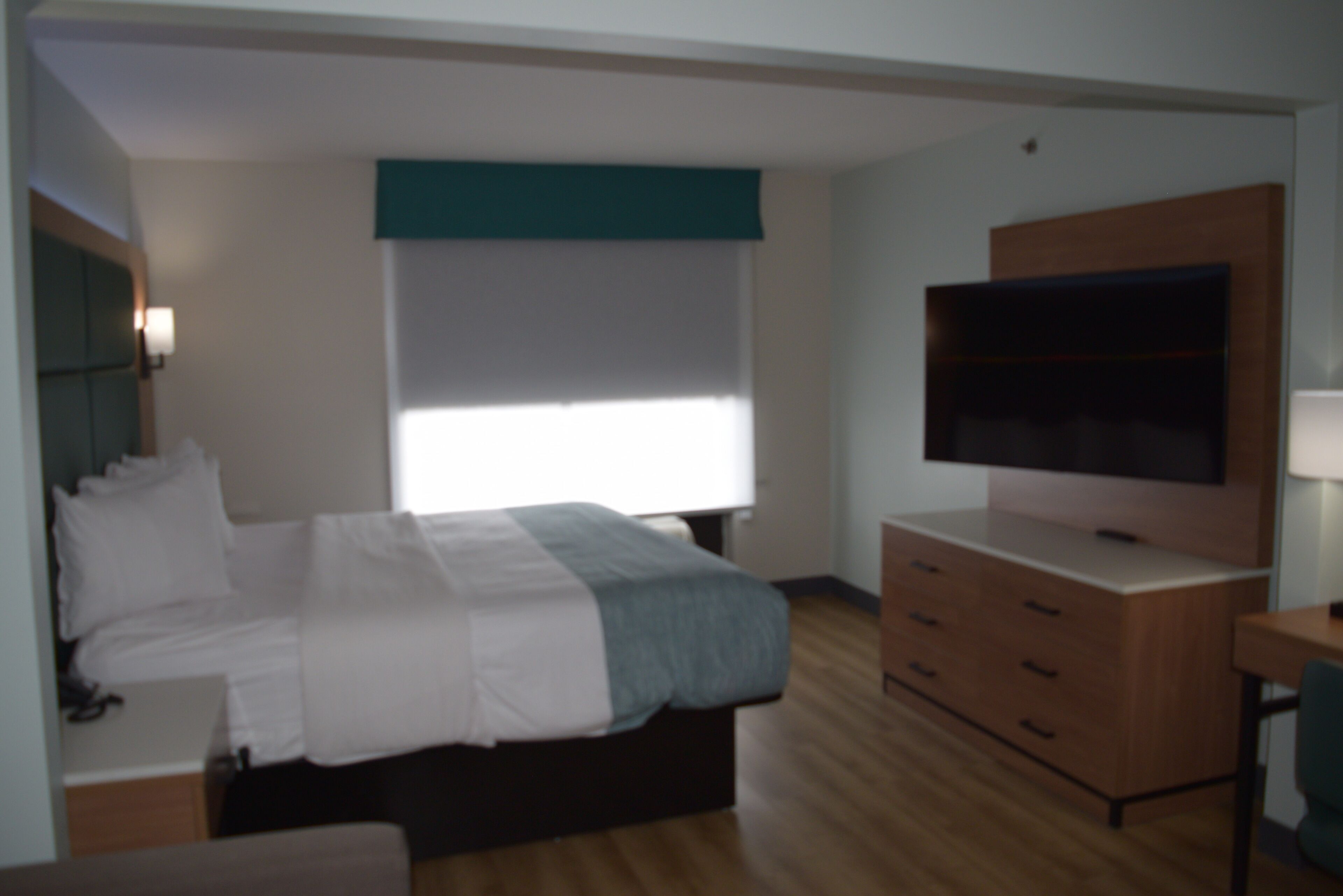Un dormitorio con cama, televisor, cómoda y ventana.