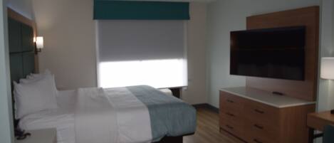 A bedroom with a bed, a TV, a dresser, and a window.
