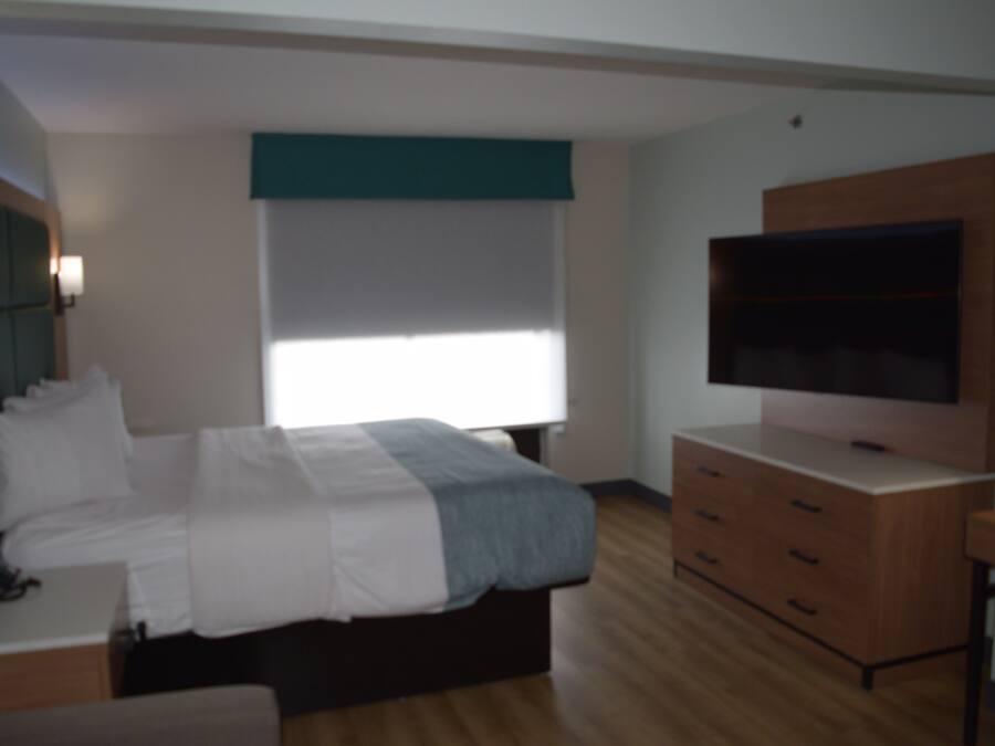 Un dormitorio con cama, televisor, cómoda y ventana.