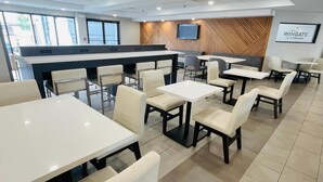 A modern dining area with a counter, multiple tables and chairs, and a mounted television. - Wingate by Wyndham Vienna/Parkersburg/Marietta (Vienna)