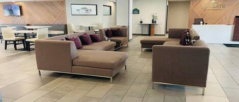 A modern hotel lobby with seating areas, a reception desk, and a mounted television.