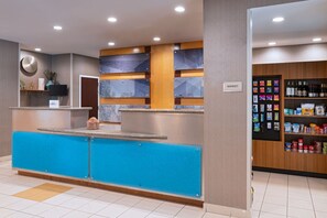 Un espace d’accueil d’hôtel avec un comptoir bleu, un espace dédié à la vente de divers produits et un mur orné d’affiches d’information.