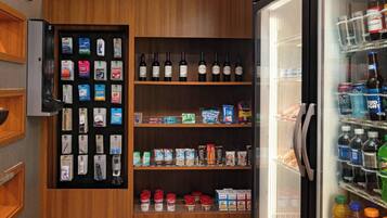 A hotel room with a minibar, a refrigerator stocked with beverages, and a shelf with snacks and condiments.