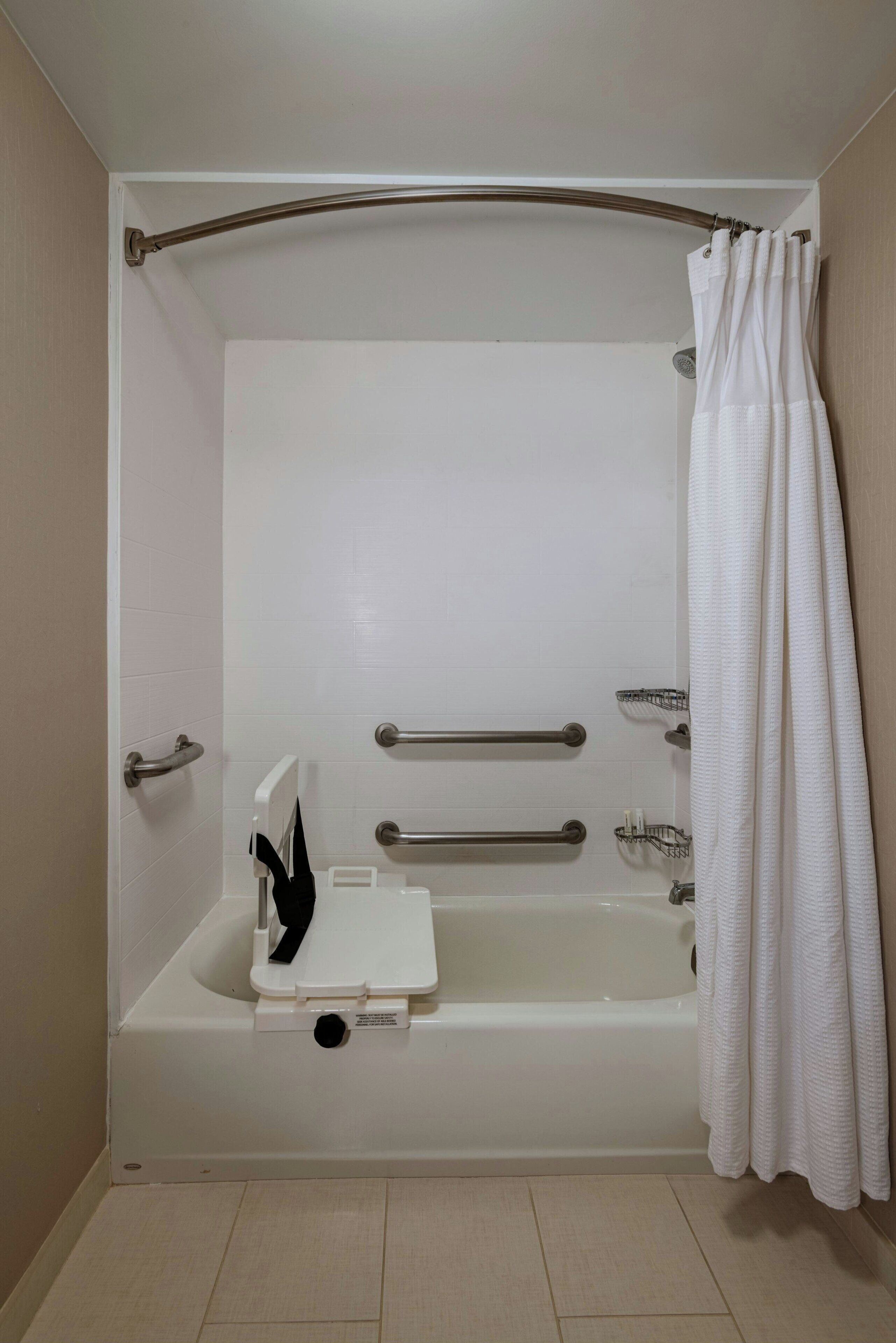 A standard bathtub with grab bars, a shower curtain, and a white tiled floor.