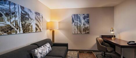 A modern hotel room with a sofa, desk, and two wall-mounted lamps.
