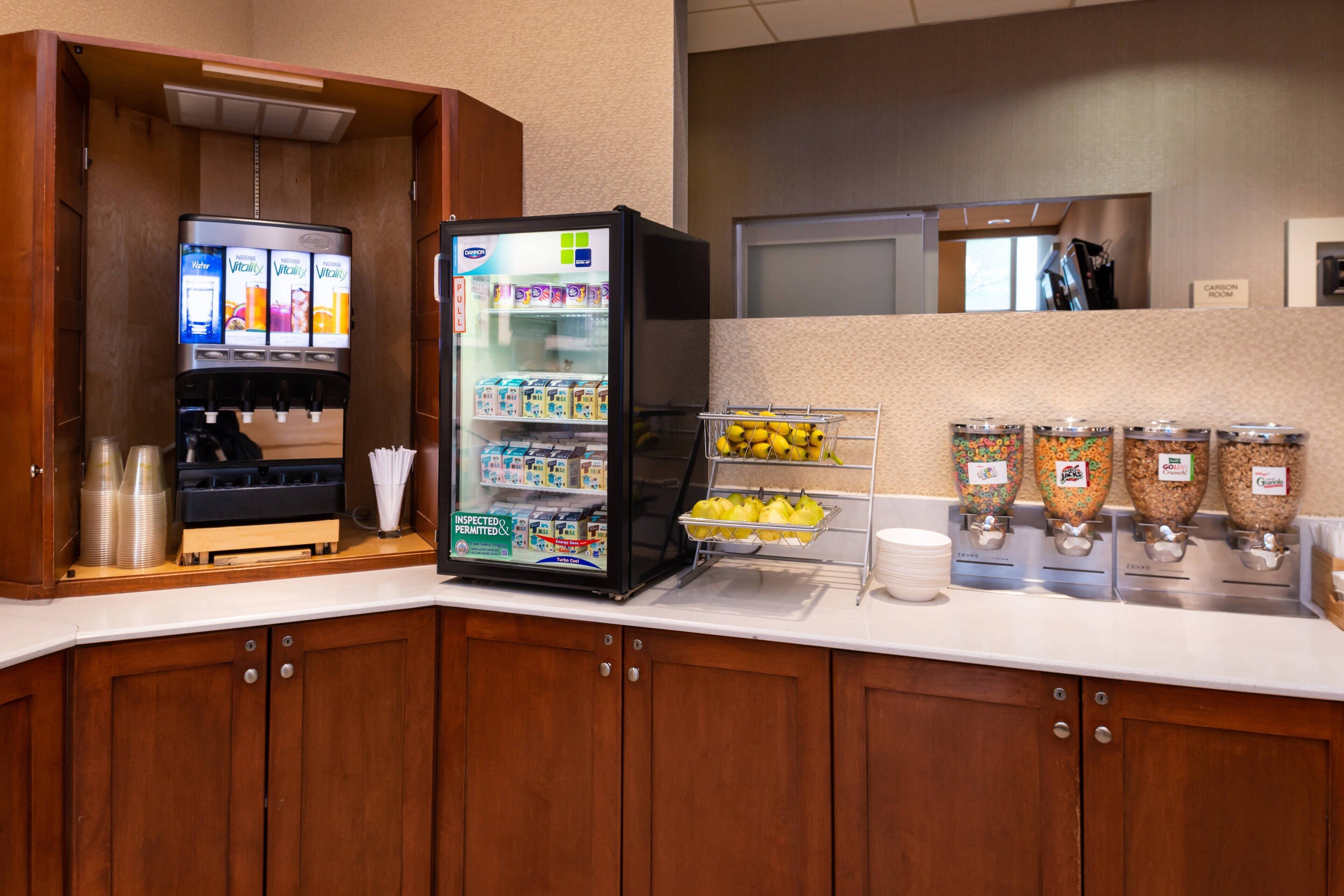 A self-service beverage station with a refrigerator and dispensers for water, juice, and coffee.