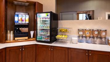 A self-service beverage station with a refrigerator and dispensers for water, juice, and coffee.