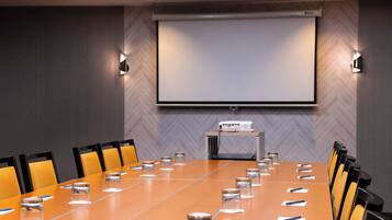 A conference room with a long table, chairs, a projector screen, and a podium.