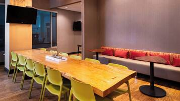 A modern meeting room with a wooden table, green chairs, a sofa with red cushions, and a television mounted on the wall.