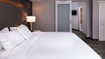 Una habitación de hotel con una cama grande, una lámpara de noche, un televisor en la pared y una puerta corredera que da al baño.