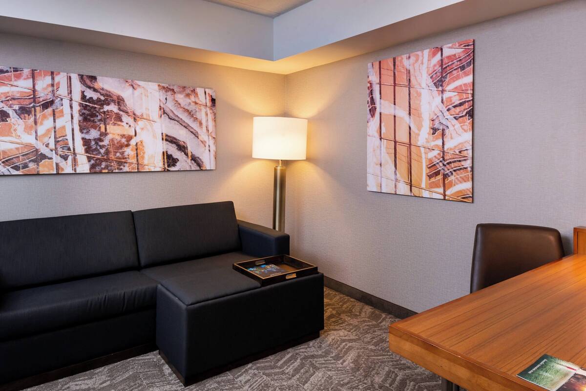 A modern hotel room with a black sofa, a wooden table, and abstract artwork on the walls.