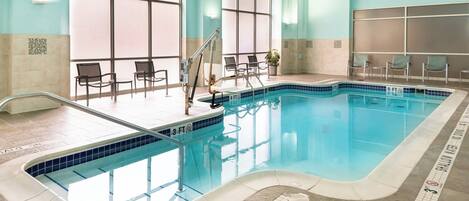 An indoor swimming pool with clear water, a shallow end marked '3 FT', and lounge chairs around the pool.