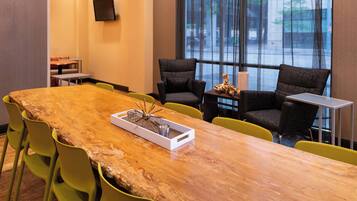 A conference room with a long wooden table, green chairs, and a large window with a view of trees and buildings.