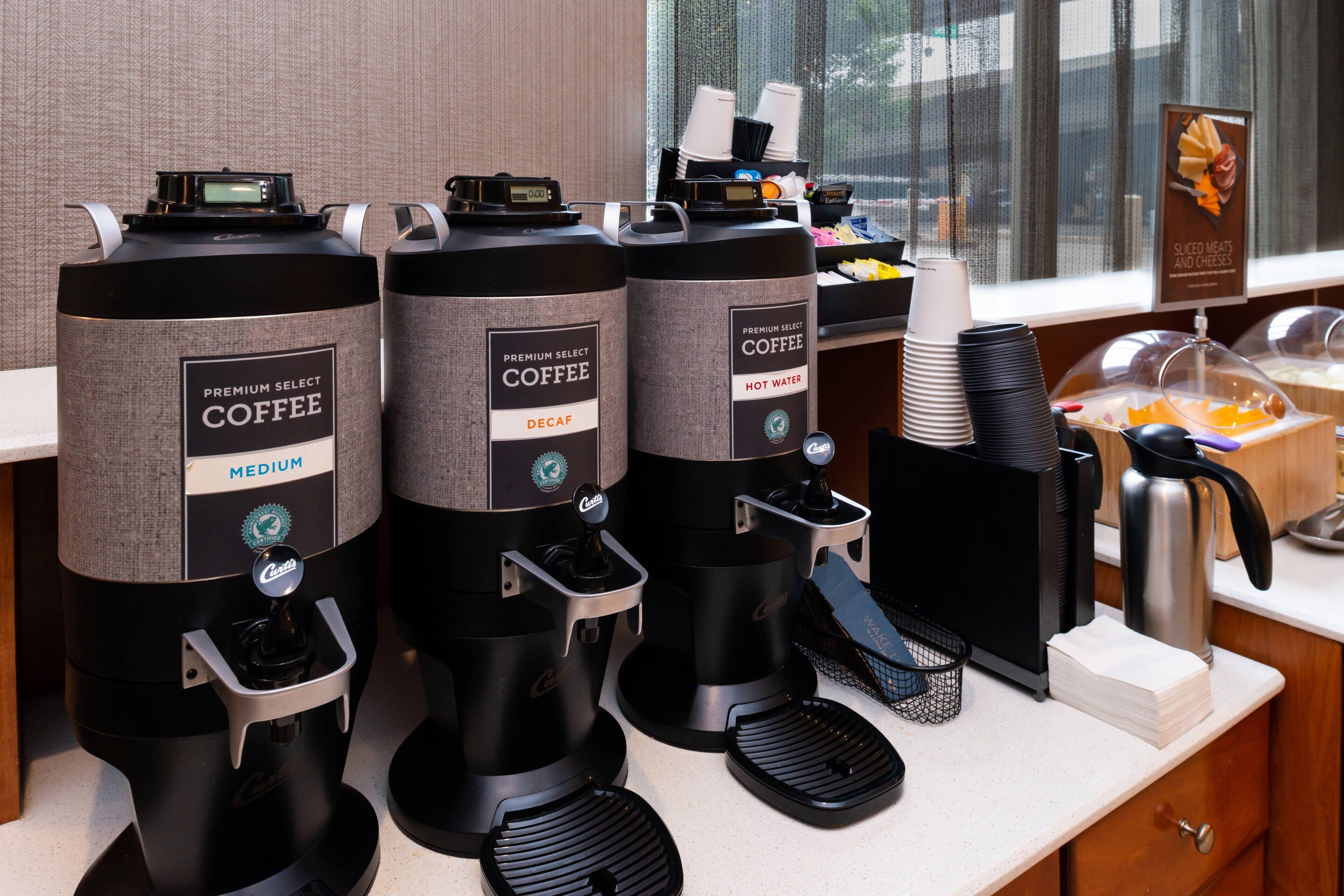 Tre distributori di caffè con l'etichetta 'Premium Select Coffee' su un bancone con vista sulla finestra.