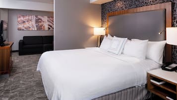 A hotel room with a large bed, a flat-screen TV, a sofa, and a patterned wall.